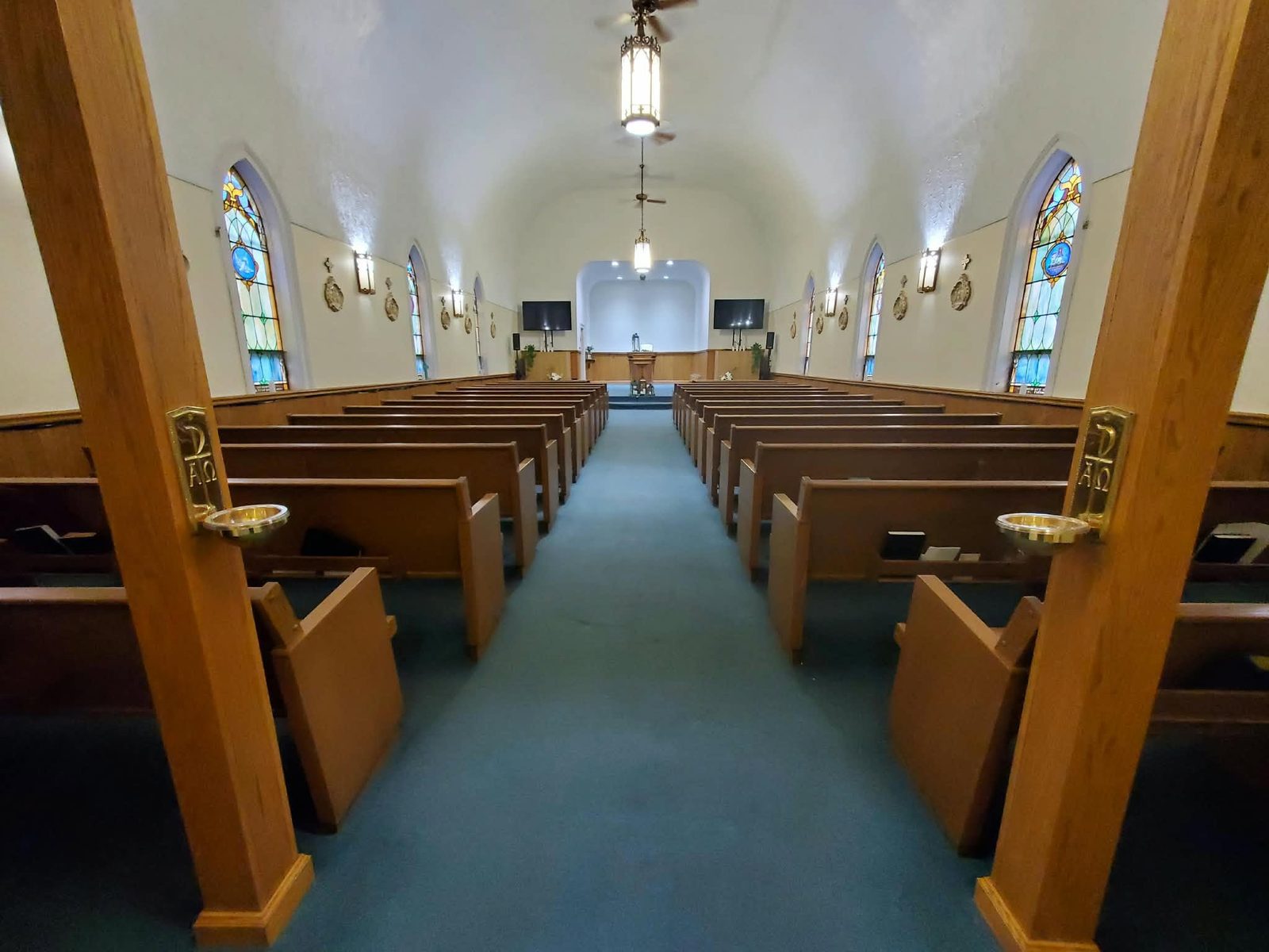 The sanctuary at True Freedom Reformed with pews, blue carpet and stained-glass windows